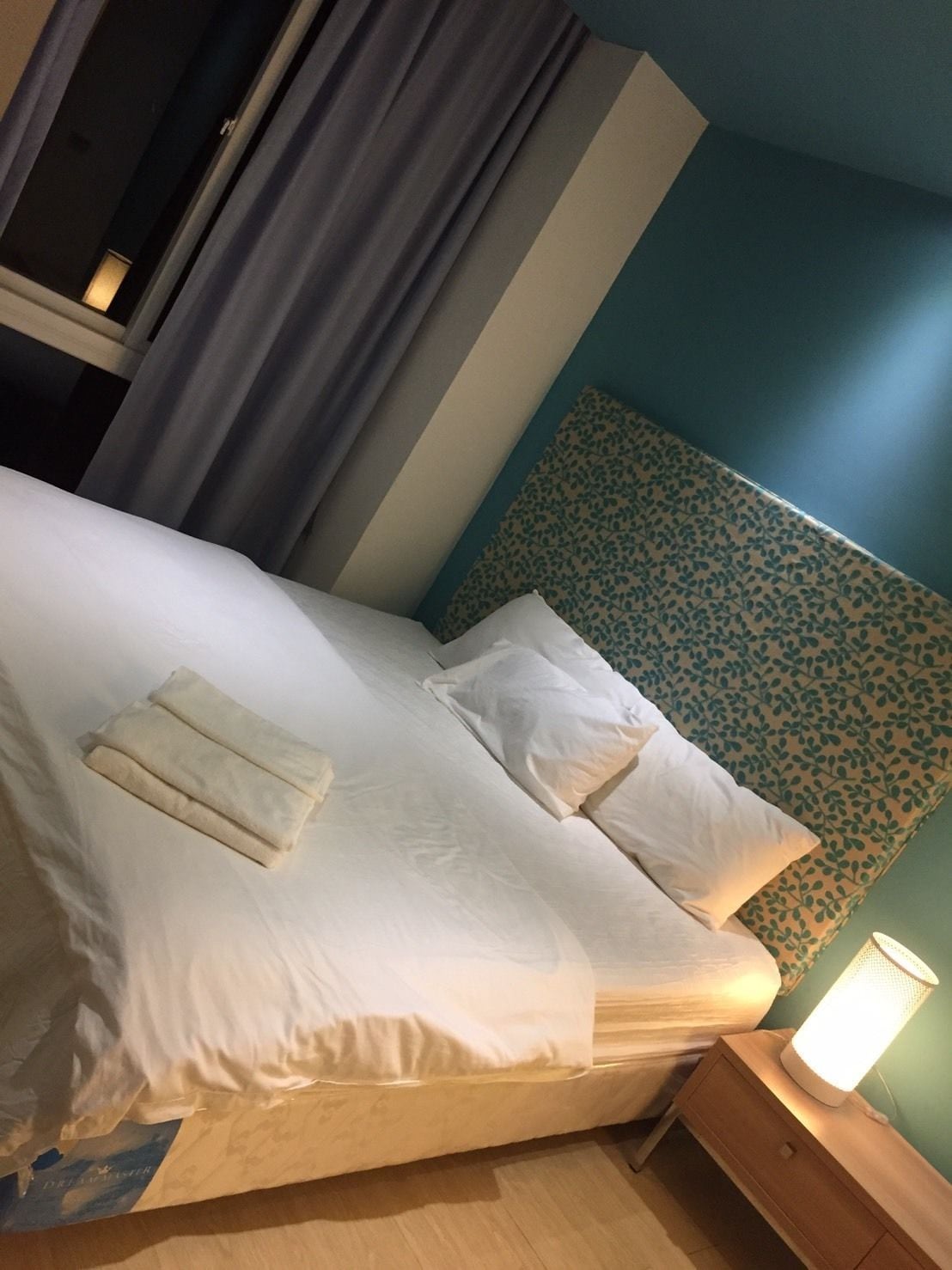 A neatly made bed with pillows and folded blankets, a bedside table with a lamp, and a patterned headboard.