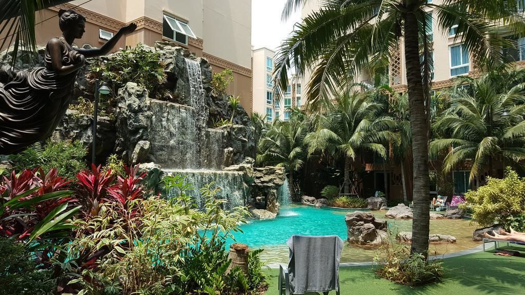 A pool area with a waterfall, palm trees, and a statue.