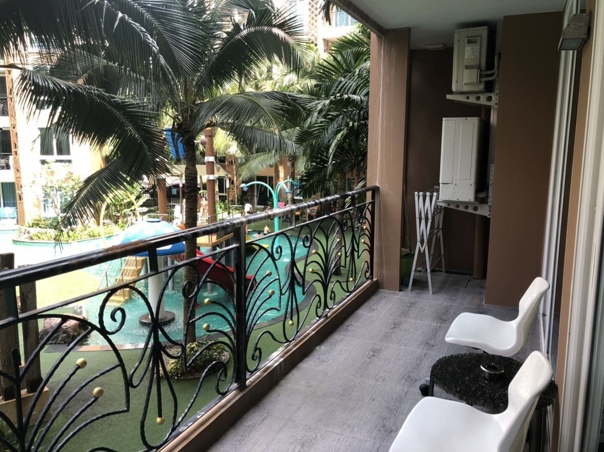 A balcony with a decorative metal railing, a small pool with a slide, and a view of palm trees and buildings.