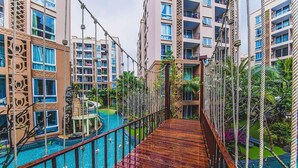 Un hotel de varios pisos con balcones, una zona de piscina y un puente de madera.