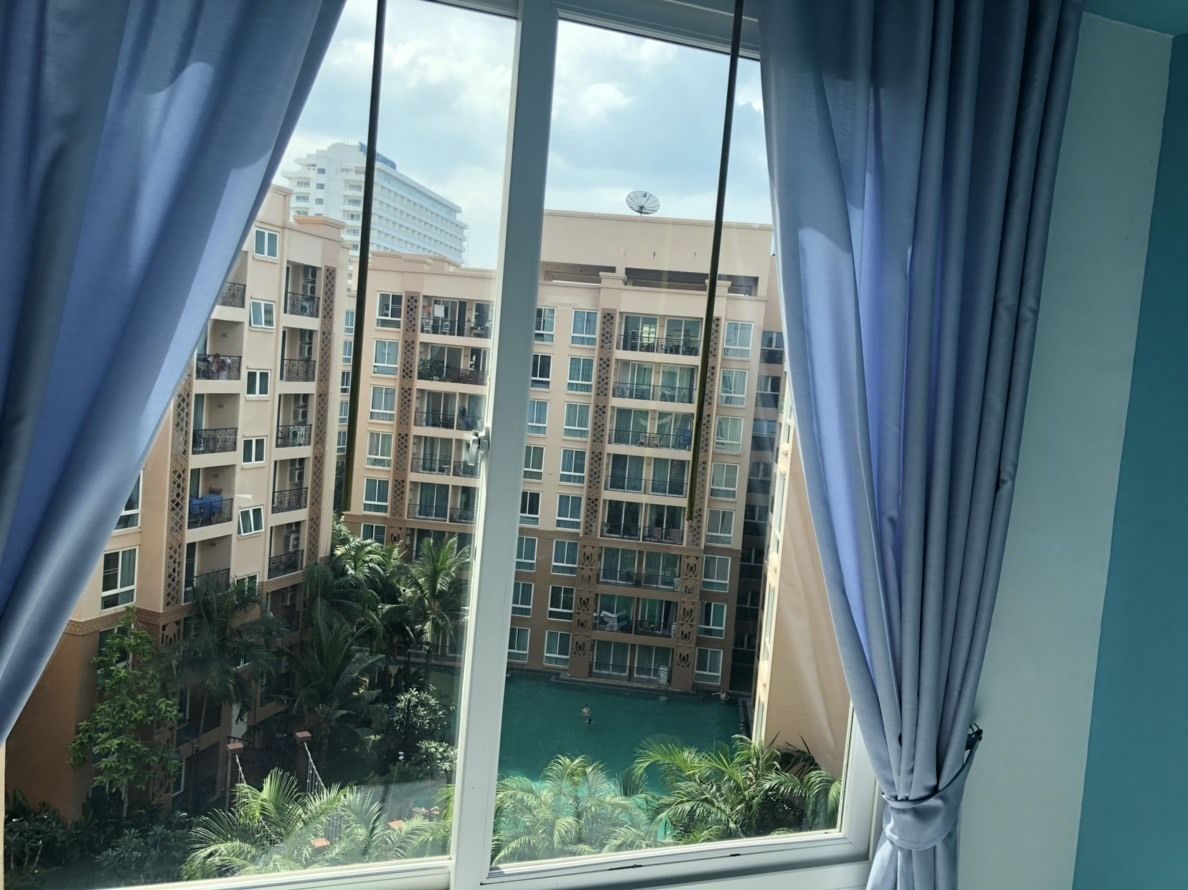 Vista desde una ventana con cortinas, que da a un edificio de varios pisos con balcones y una piscina.