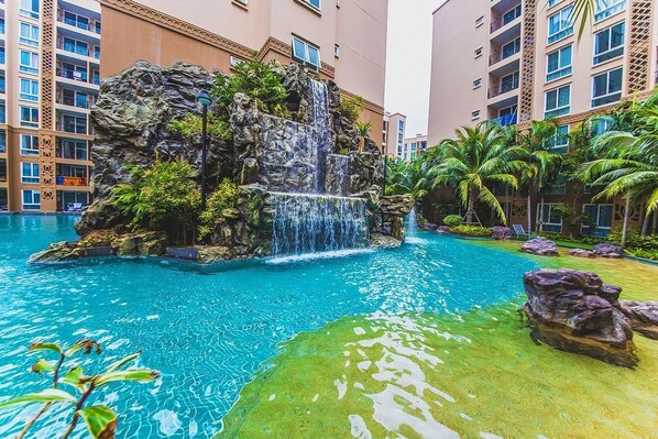 Piscina de hotel con caída de agua rodeada de exuberante vegetación y palmeras.