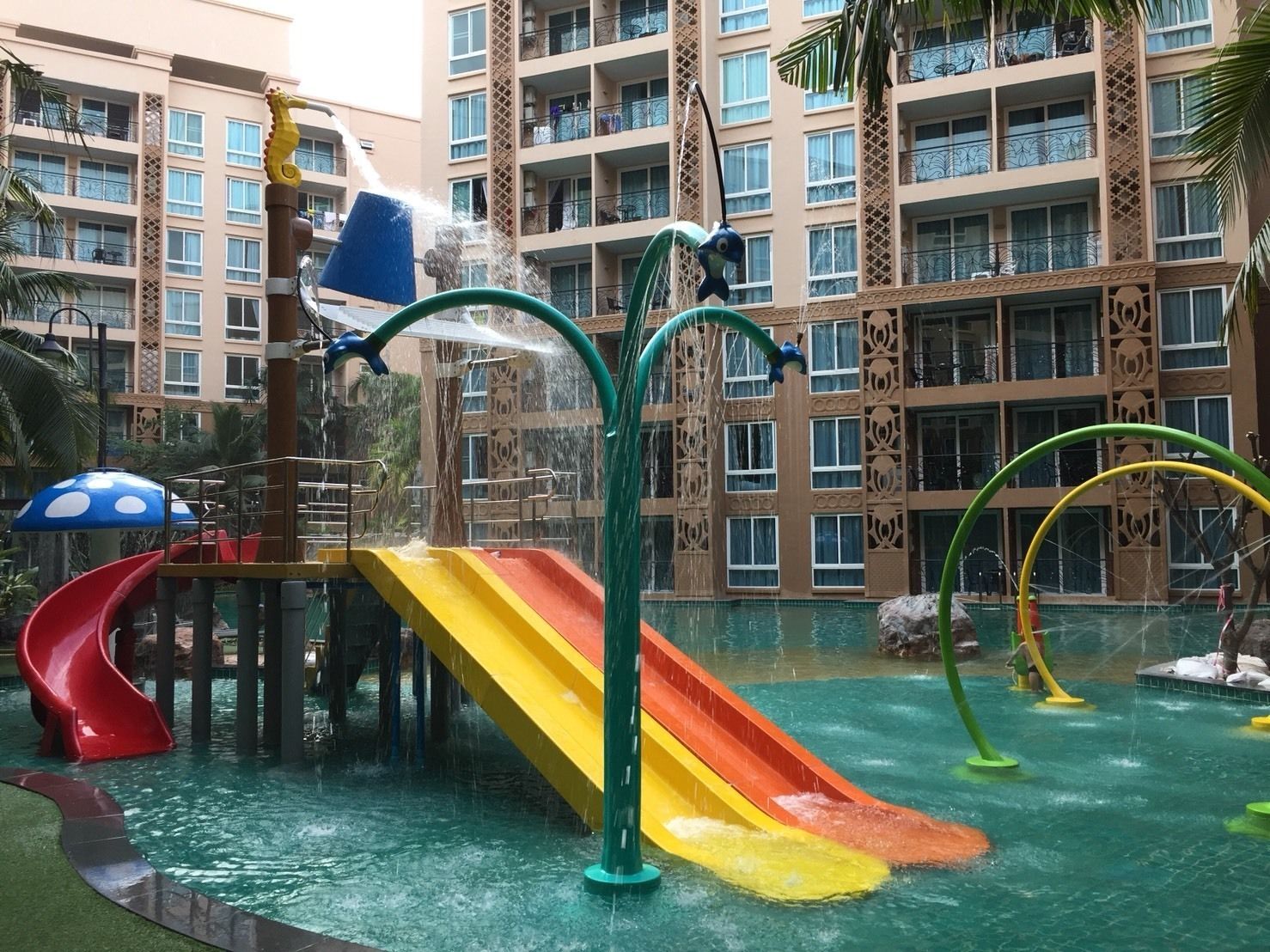 A water park area with slides and water features, surrounded by a multi-story building with balconies.