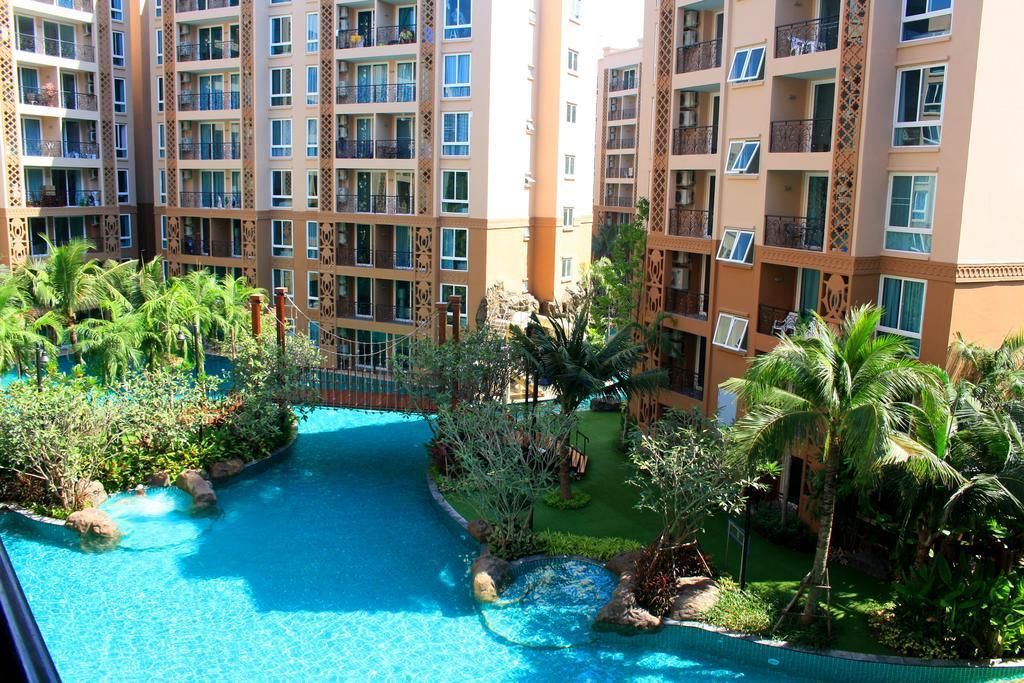 Um hotel com vários andares, piscina central rodeada por vegetação exuberante e palmeiras.