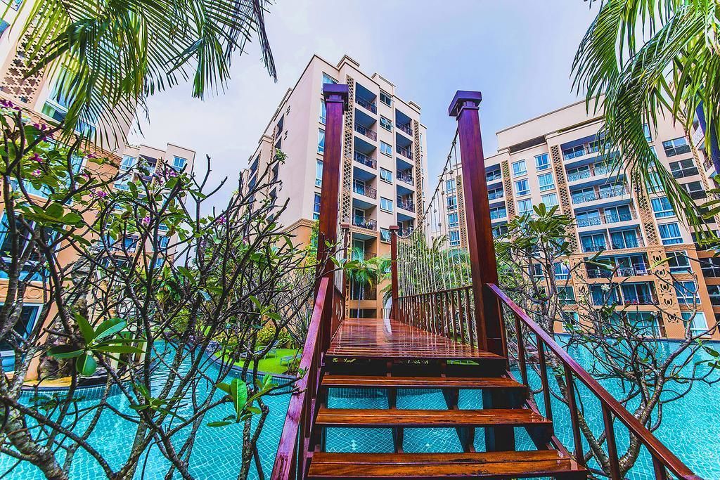 A wooden staircase leading to a swimming pool surrounded by tall buildings and palm trees.