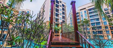 A wooden staircase leading to a swimming pool surrounded by tall buildings and palm trees.