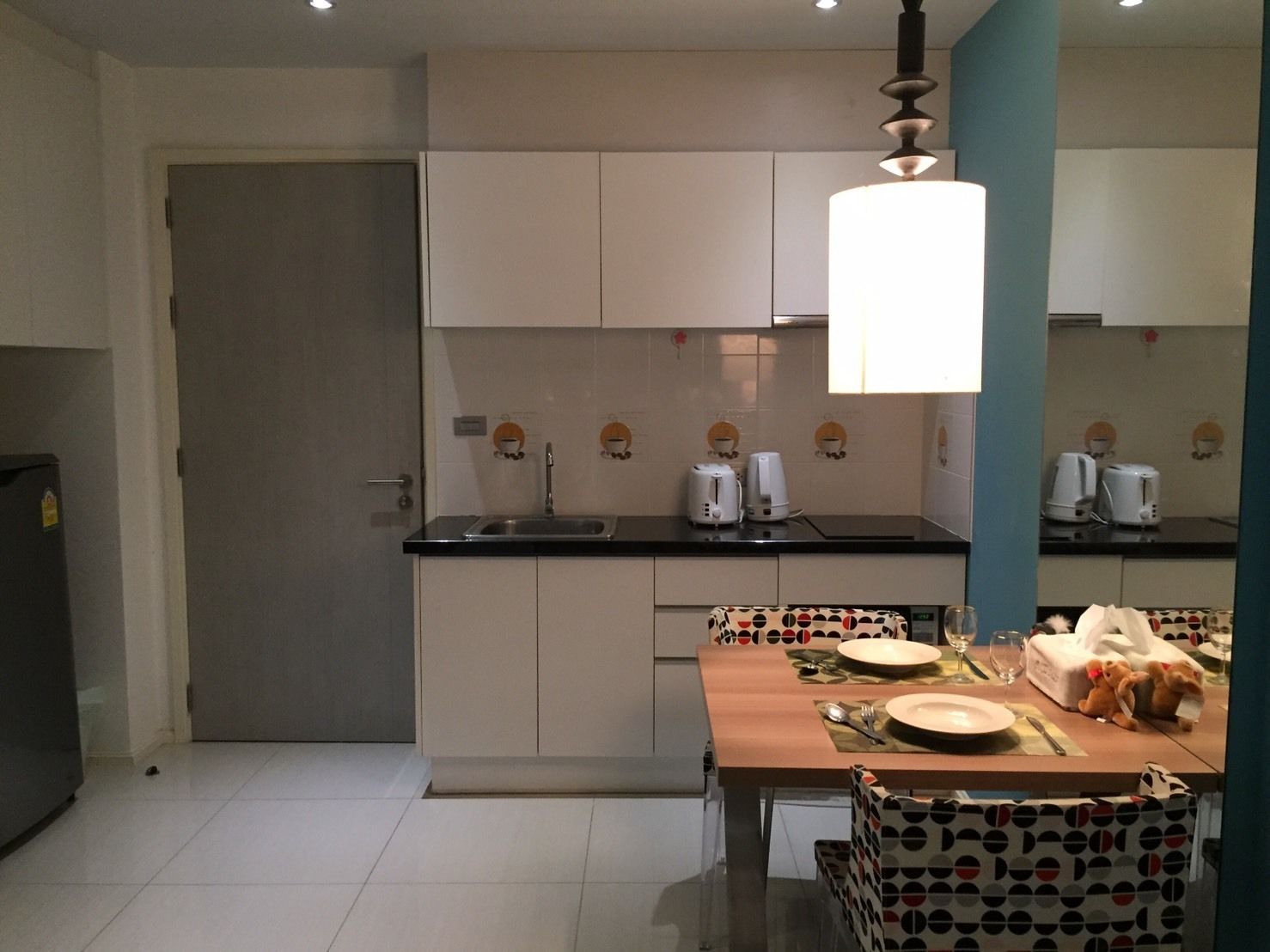 A compact kitchen with a dining area, featuring a sink, countertop, and a dining table set with plates and cutlery.