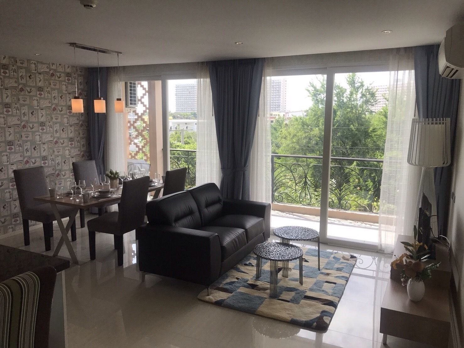 Een moderne woonkamer met een bank, eettafel, stoelen en een balkon met uitzicht op groen en gebouwen.