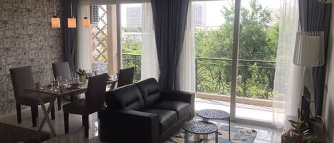 Een moderne woonkamer met een bank, eettafel, stoelen en een balkon met uitzicht op groen en gebouwen.