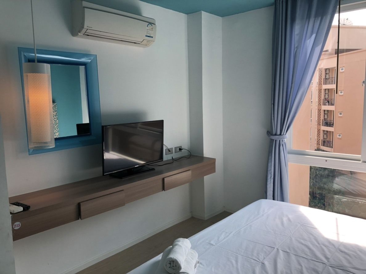 Une chambre d’hôtel avec un lit, un téléviseur posé sur une étagère en bois, un miroir et un appareil de climatisation.