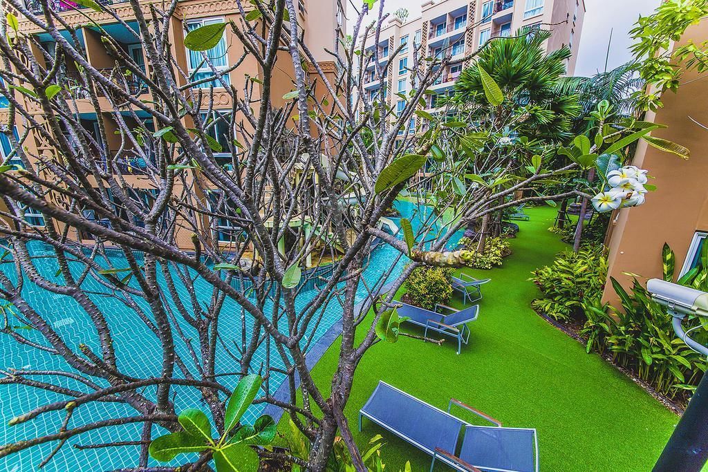 An indoor swimming pool surrounded by artificial grass, with lounge chairs and a variety of tropical plants.