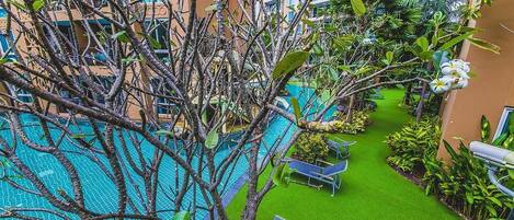 An indoor swimming pool surrounded by artificial grass, with lounge chairs and a variety of tropical plants.