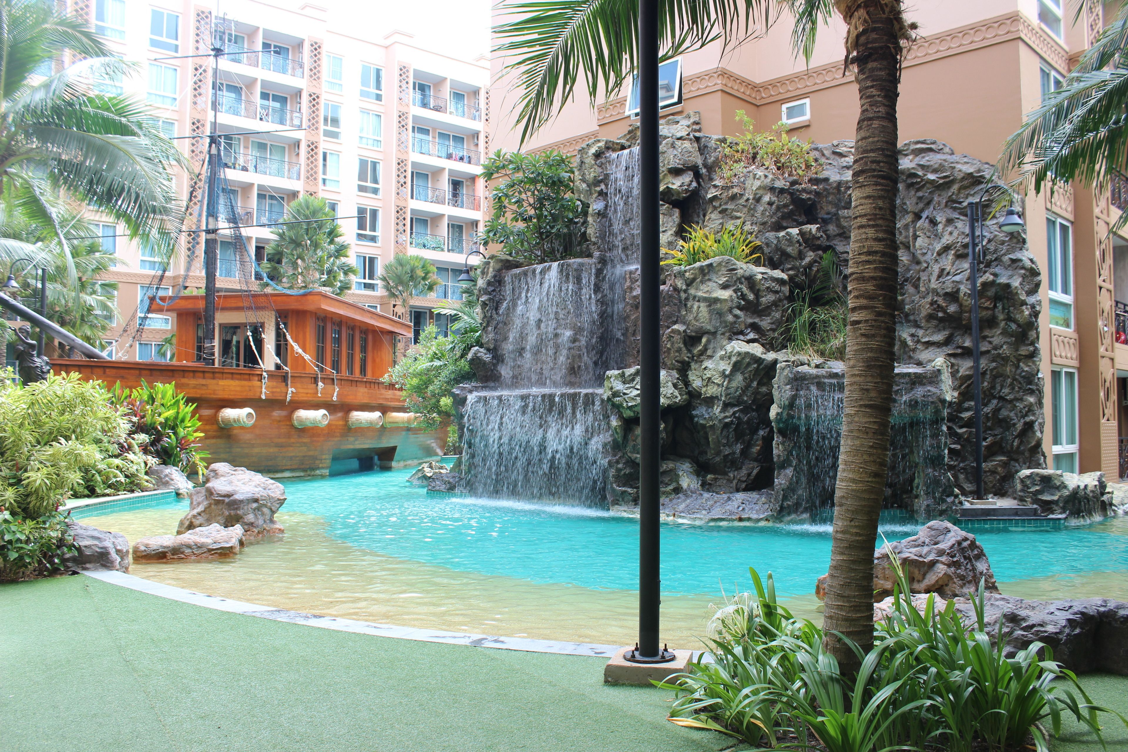 A hotel pool area with a waterfall, palm trees, and a ship-themed building.