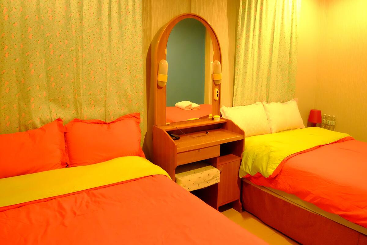 Habitación de hotel con dos camas, un escritorio de madera, un espejo y un estante pequeño.