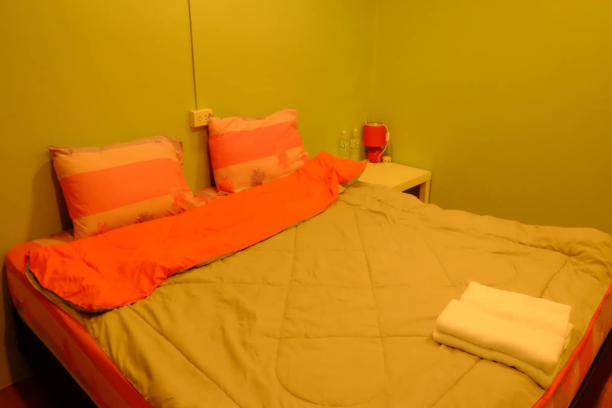 Una cama con una manta color beige y naranja, dos almohadas y una toalla blanca.