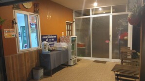 A room with a tiled floor, a table with a blue tablecloth, a refrigerator, a bench, and a window with a view of the outside. - Kaikatak Resort (Klaeng)