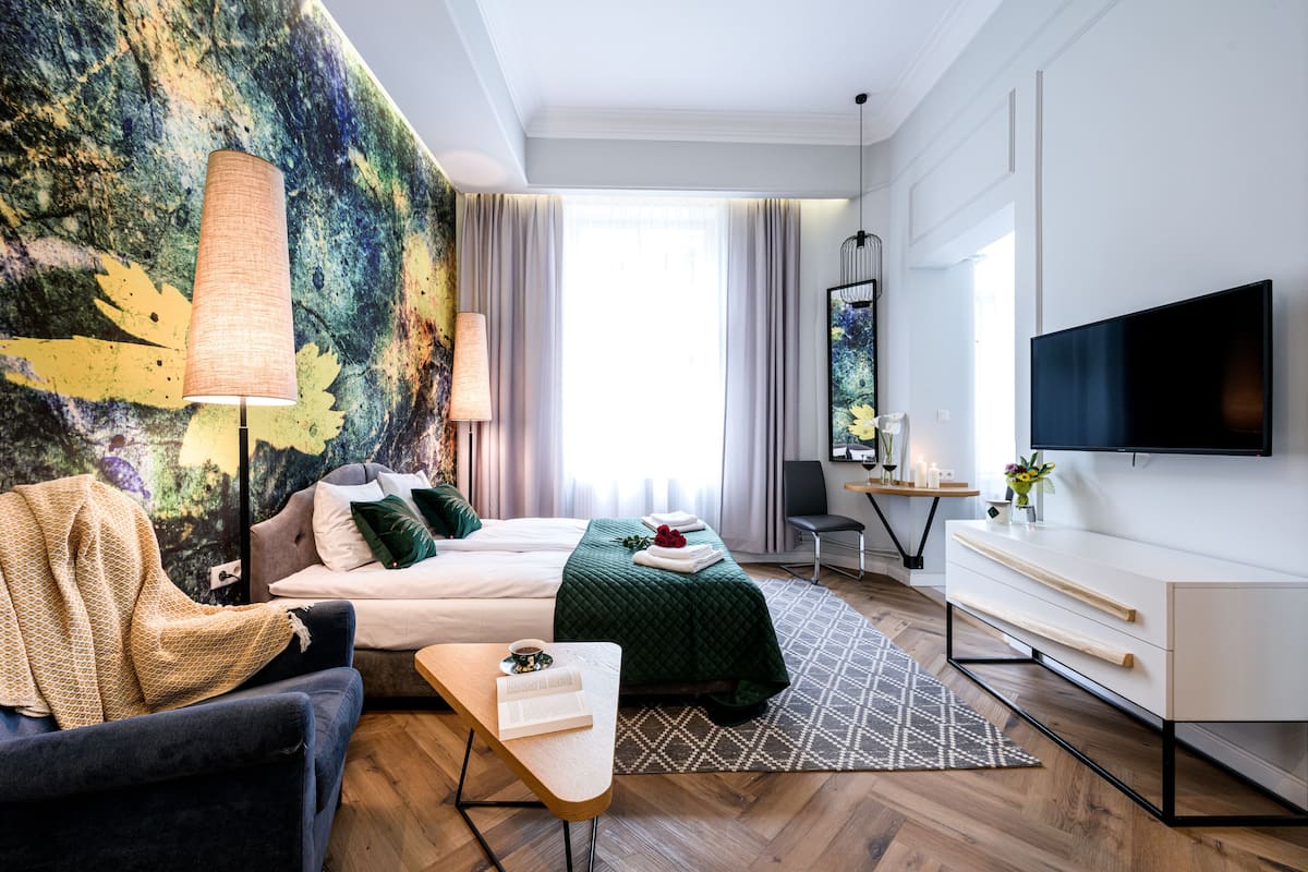 A modern hotel room with a bed, a desk, a TV, and a large abstract painting on the wall.