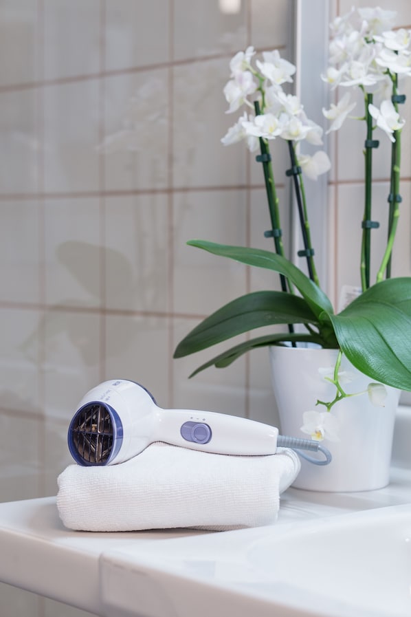 Un sèche-cheveux blanc et une serviette sur le comptoir d’une salle de bain, avec une orchidée en pot en arrière-plan.