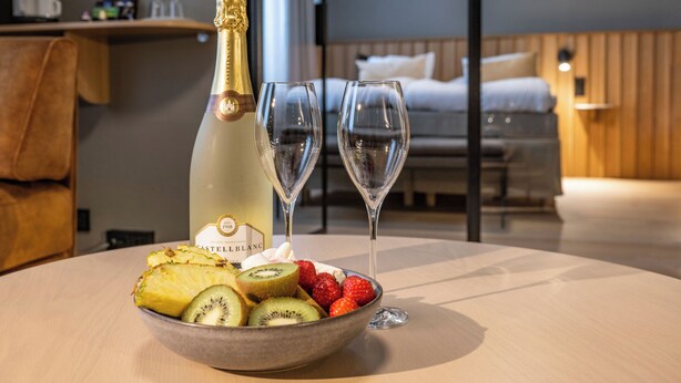 A hotel room with a wooden bed, a bedside table with a bottle of champagne and two glasses, and a bowl of fruit on the table. - Park Hotel Tornio (Tornio)