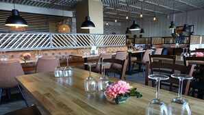 A restaurant with wooden tables, cushioned seating, and pendant lighting. - Park Hotel Tornio (Tornio)