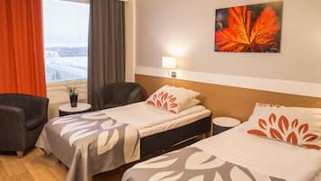 A hotel room with two beds, a desk, a chair, a window with curtains, a wall-mounted lamp, and a painting of a leaf.