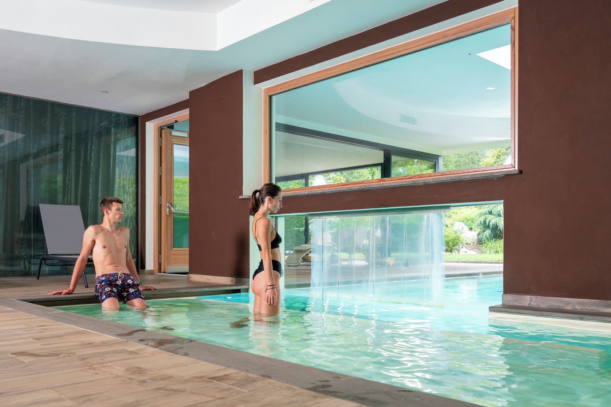 Piscina interna moderna con ampie finestre e vista sul verde circostante.