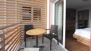Un balcon doté d’un mur en lattes de bois, une table ronde, deux chaises et un lit dans la pièce adjacente.