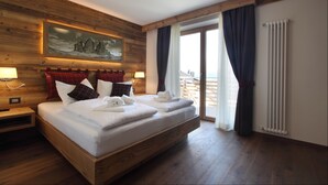 Un lit double avec du linge de lit et des serviettes blanches, une tête de lit en bois, un tableau au-dessus du lit, une table de chevet avec une lampe et une grande fenêtre avec des rideaux.