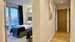 A modern hotel room with a large bed, a view through a sliding glass door, and a wooden floor. - Your Space Apartments - The Hamilton's (Cambridge)