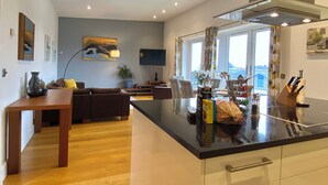 A modern kitchen with a central island, dining area with a sofa, and a large window providing a view. - Your Space Apartments - The Hamilton's (Cambridge)
