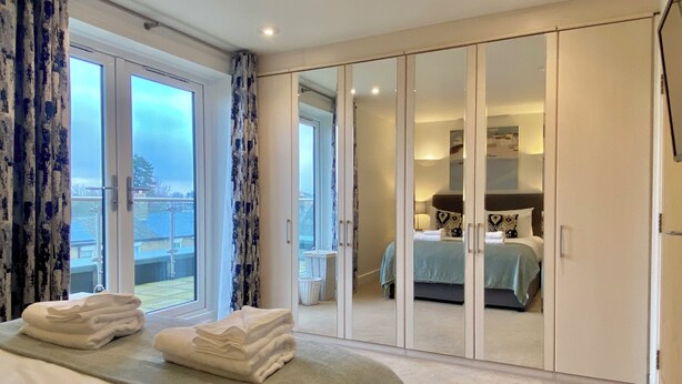 A bedroom with a bed, a wardrobe, a balcony, and a view of the outside. - Your Space Apartments - The Hamilton's (Cambridge)