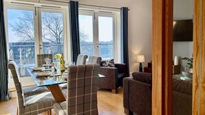 A dining area with a glass table, chairs, and a view of trees outside. - Your Space Apartments - The Hamilton's (Cambridge)