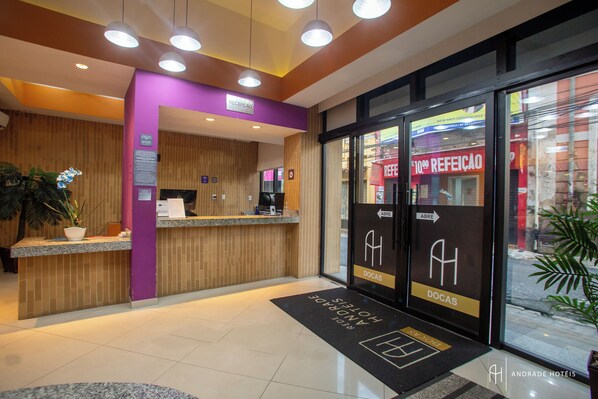 Un espace d’accueil d’hôtel comprenant un comptoir de réception, un mur violet et un panneau indiquant « Réception ».