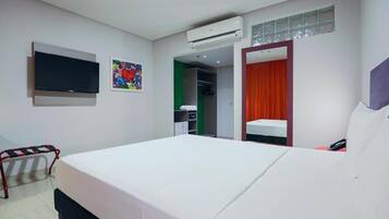 Habitación de hotel con cama, televisor, armario y baño visible a través de una puerta abierta.