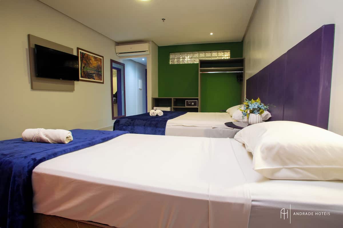 A hotel room with two beds, a flat-screen TV, an air conditioning unit, and a green accent wall.