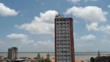 Un edificio alto con fachada roja y numerosas ventanas, rodeado de otros edificios con tejados de tejas rojas.