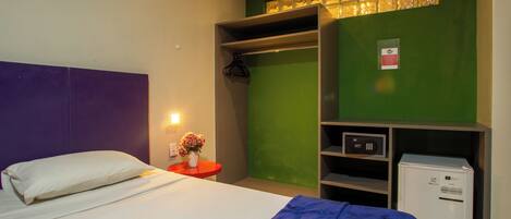 Habitación de hotel con cama, una mesita de noche roja con un florero, pared verde, armario y minibar.