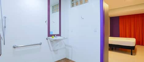 A bathroom with a shower, a sink, a mirror, and a toilet. There is a red curtain in the adjacent room.