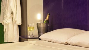 A hotel room with a bed, a nightstand with a bottle of champagne and glasses, and a robe hanging on the wall. - Rede Andrade Docas (Belém)