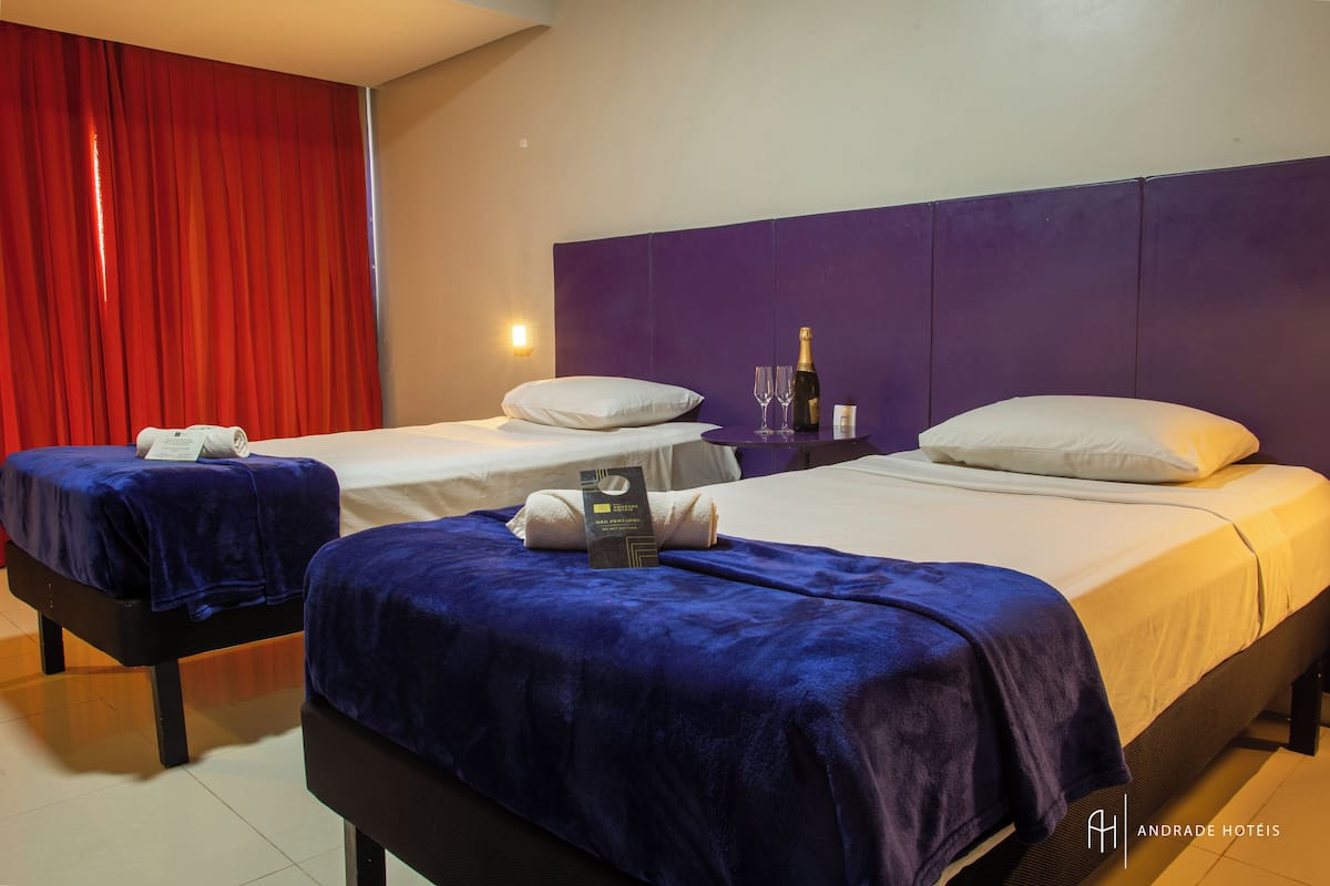 A hotel room with two beds, each with a blue blanket, white pillows, and a bottle of champagne.