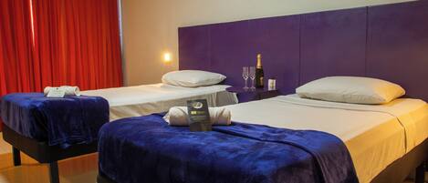 Une chambre d’hôtel avec deux lits, chacun recouvert d’une couverture bleue, agrémenté d’oreillers blancs et d’une bouteille de champagne.