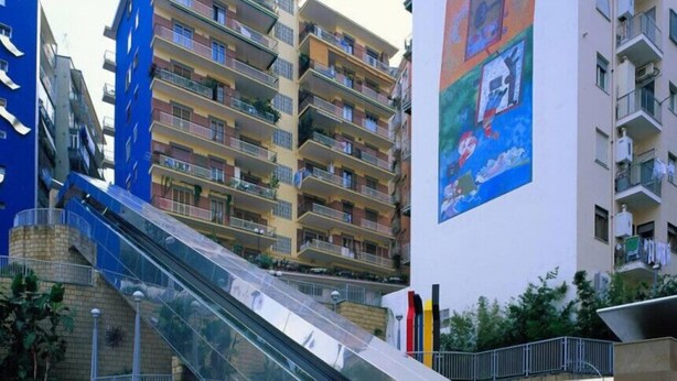 A multi-story residential building with balconies, a central staircase, and a large mural on the wall. - I Colori di Salvator Rosa (Naples)