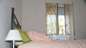 A bedroom with a bed, a lamp, and a window with floral curtains. - I Colori di Salvator Rosa (Naples)