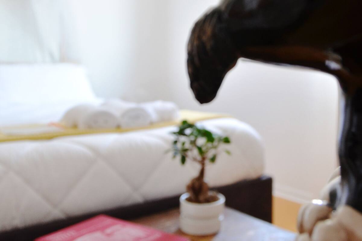 A bed with a white quilt, a small potted plant, and a decorative horse head sculpture.