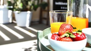 A table with a bowl of strawberries and a glass of orange juice, a bottle of water, and a chair in a sunny outdoor setting. - Lo spazio di Mima (Noto)