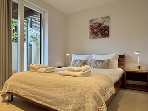 Quarto com cama, duas mesas de cabeceira, um quadro e vista através de uma porta de correr.