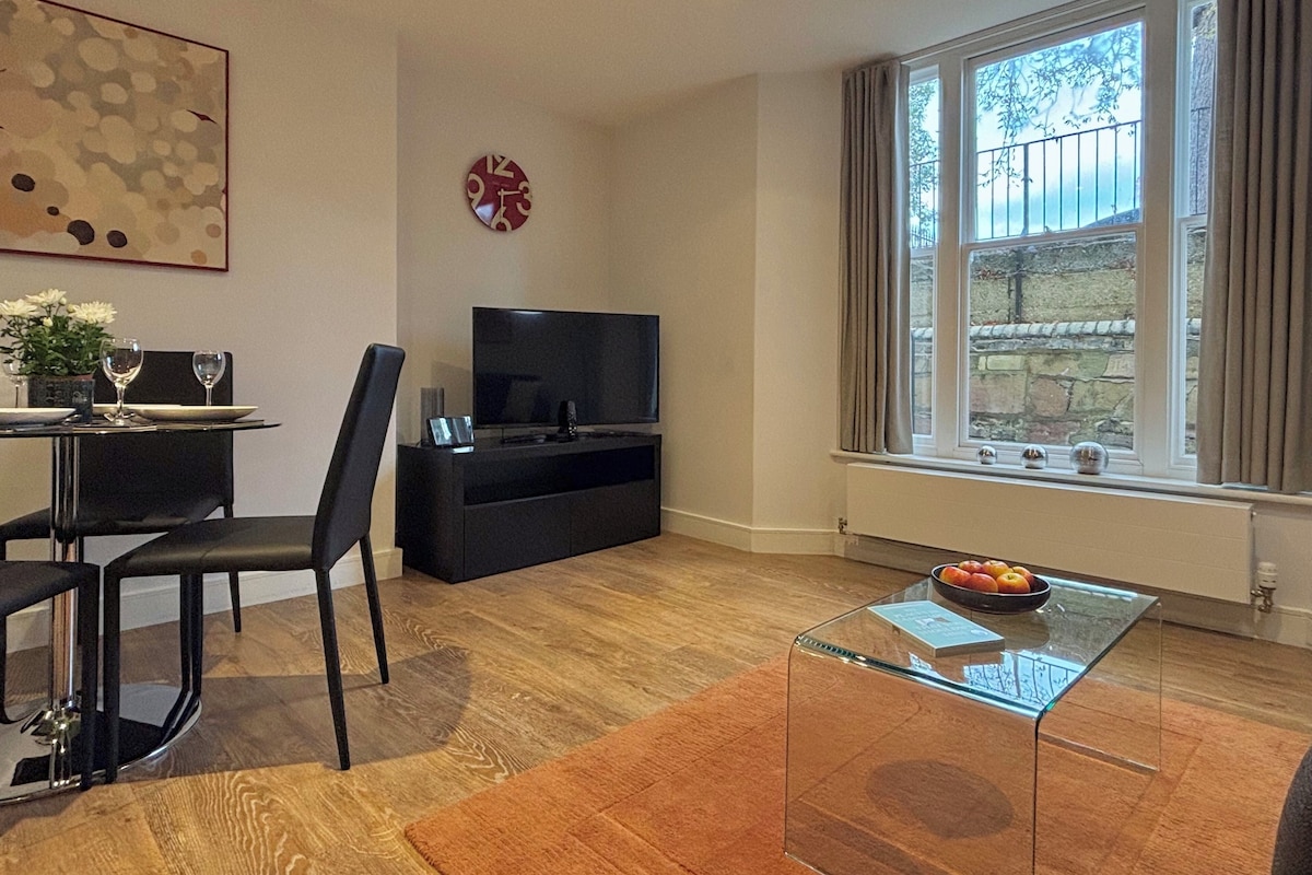 Una sala de estar moderna con comedor, televisor de pantalla plana, un ventanal con cortinas y un reloj decorativo.