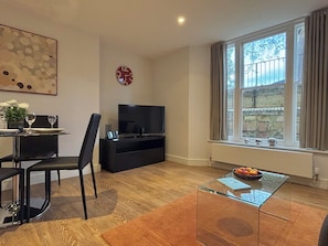 Una sala de estar moderna con comedor, televisor de pantalla plana, un ventanal con cortinas y un reloj decorativo.