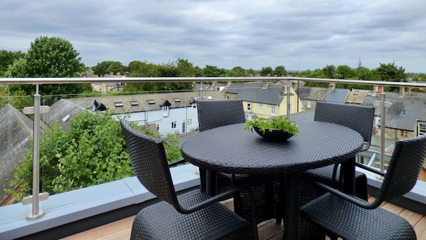 A balcony with a round table and four chairs, overlooking a residential area with houses and trees. - Your Space Apartments - Jubilee House (Cambridge)