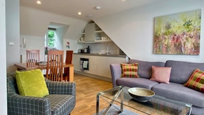 A modern living room with a sofa, a glass coffee table, and a dining area with chairs and a table. - Your Space Apartments - Jubilee House (Cambridge)